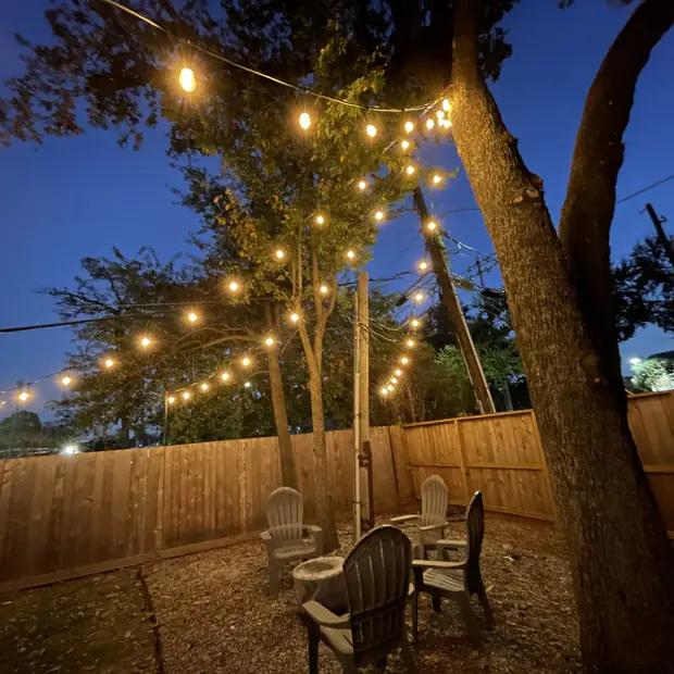 String lights spanning a backyard between a large tree and seating area