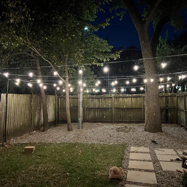 String lighting over a lawn beside a lit fence line