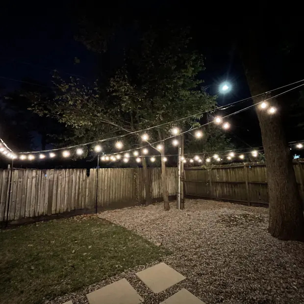Garden seating area under crossed runs of bistro lighting