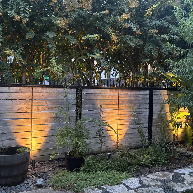 Low-voltage uplights grazing a timber fence in scalloped pools of warm light
