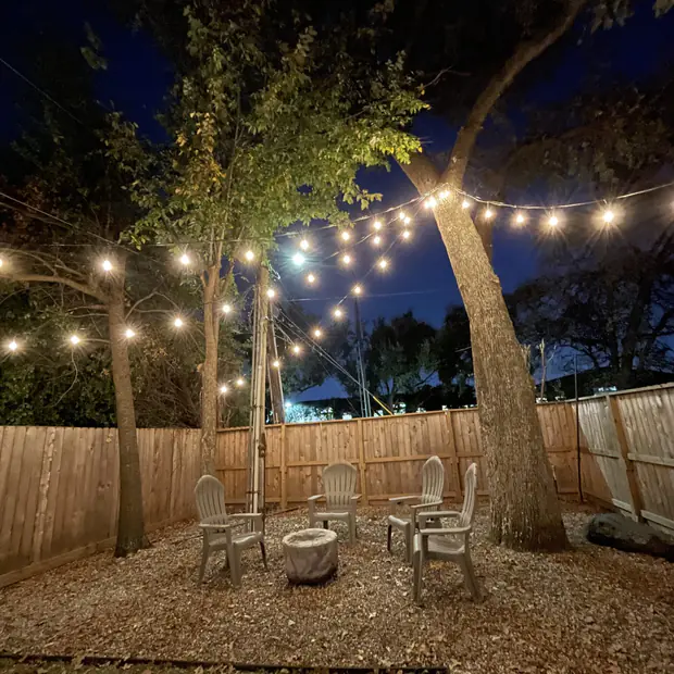Warm string lighting over a fire pit and garden seating