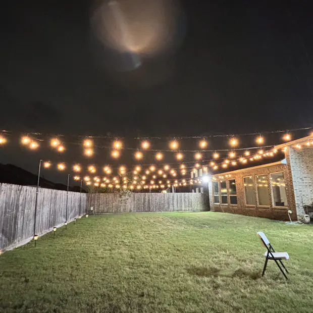 Bistro lights crossing a lawn between house and fence