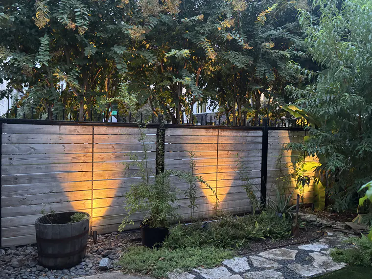 Low-voltage uplights grazing a timber fence in scalloped pools of warm light